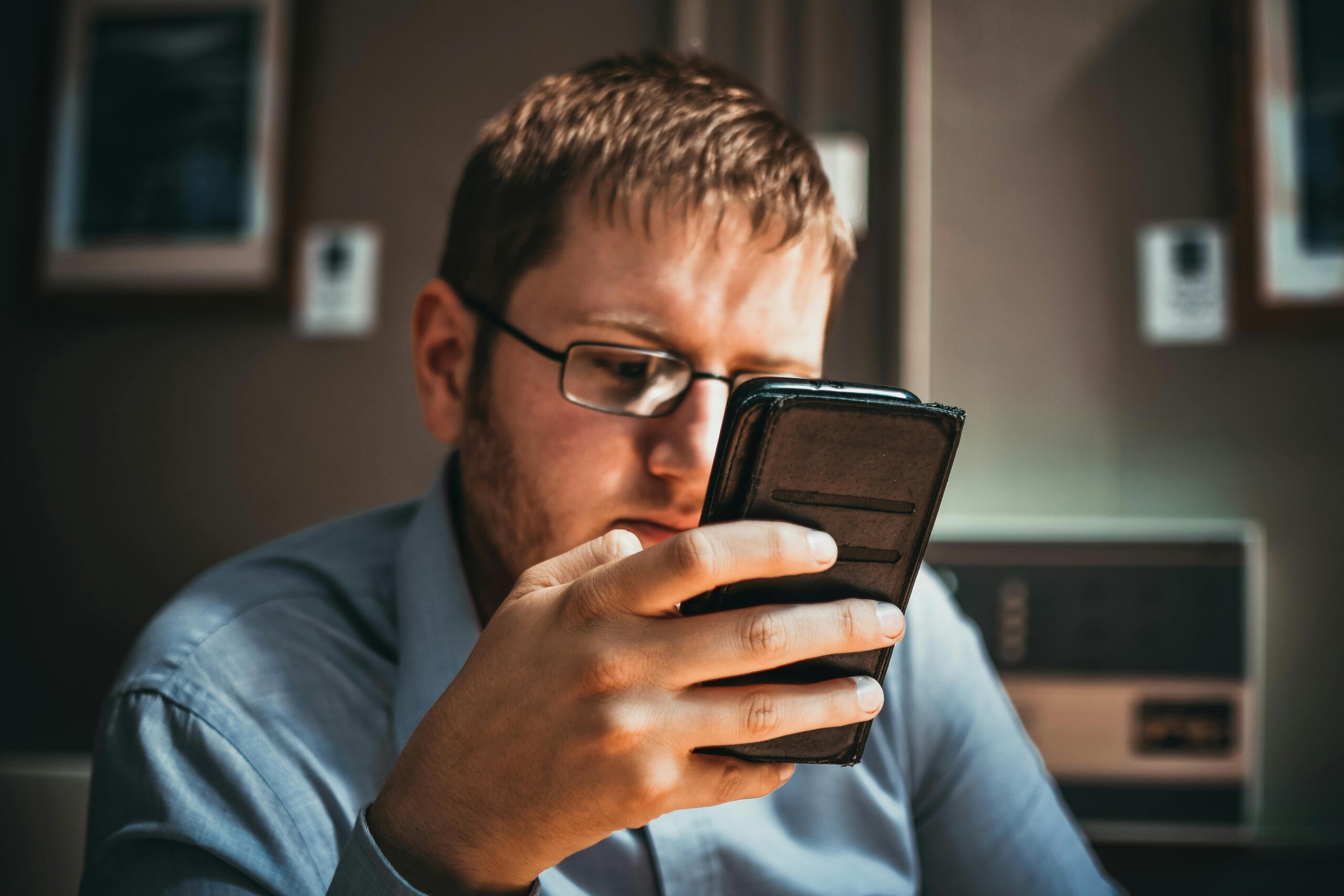 Mobile Privacy Attacks: Shocking Truths About Smartphone Serious businessman wearing glasses focused on smartphone in a modern office setting.